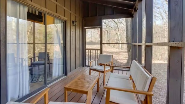Un espace extérieur aménagé, abrité et doté de mobilier en bois et de grandes fenêtres.