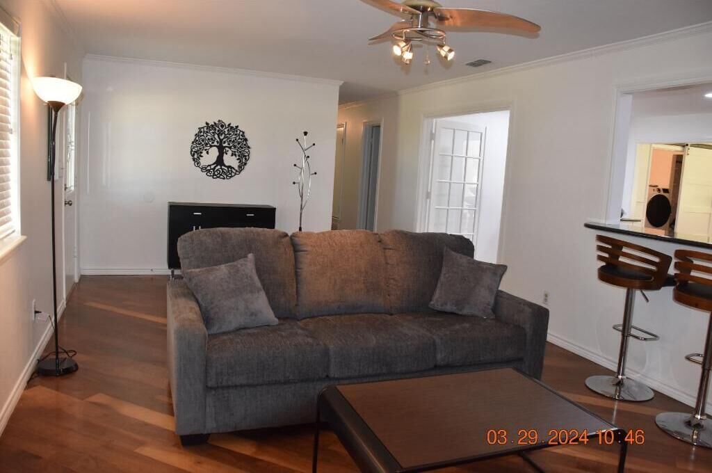 A living room with a grey sofa, a coffee table, a ceiling fan, and a bar area with stools.