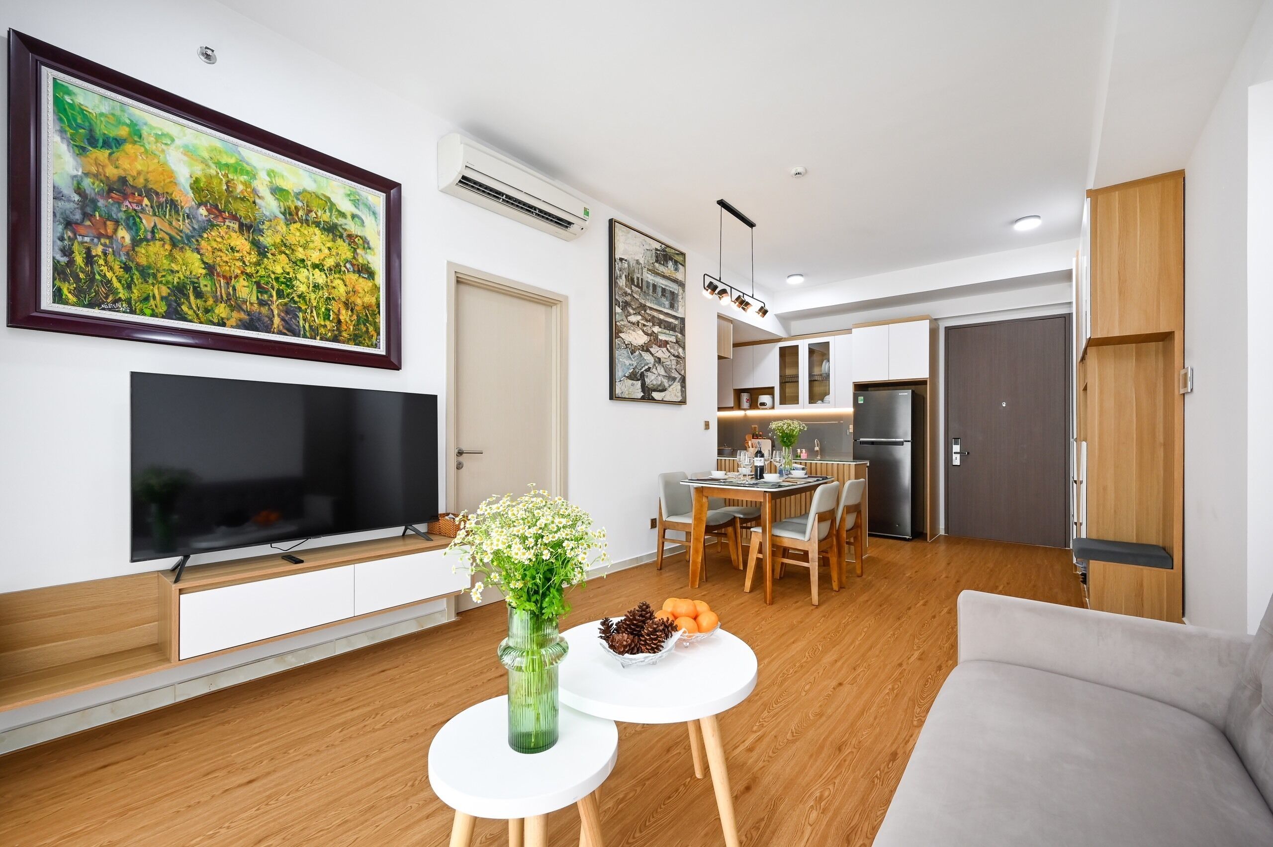 A modern living room with a flat-screen TV, a dining area with a table and chairs, and a kitchen in the background.