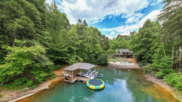 A lakeside cabin with a dock, a floating platform, and a house in the background.