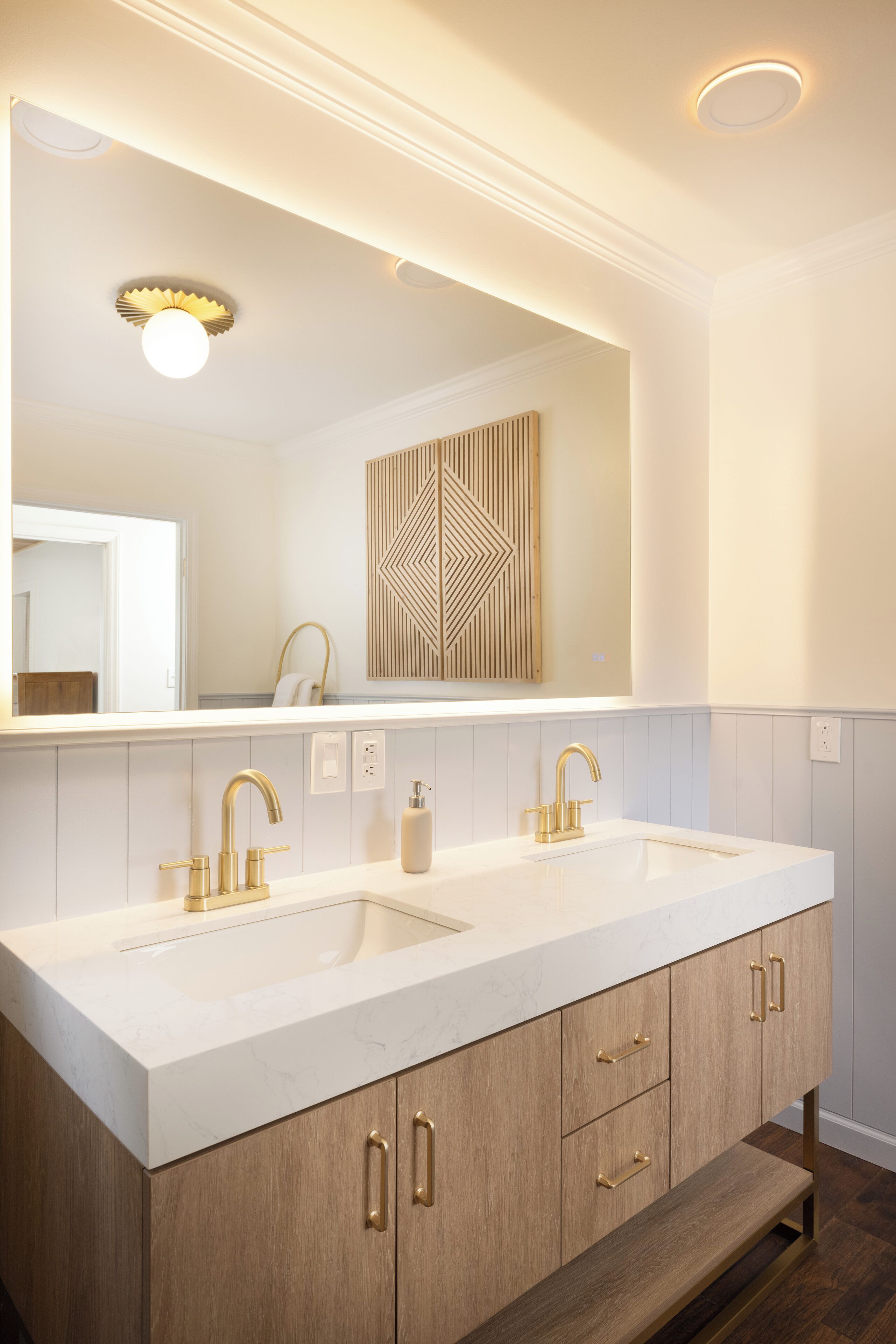 A bathroom with a large mirror, two sinks, and wooden cabinets.