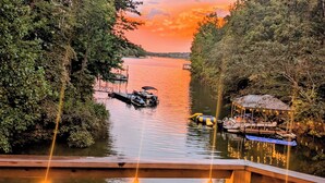 A lakeside deck with chairs and tables, overlooking a calm lake with boats and a dock.
