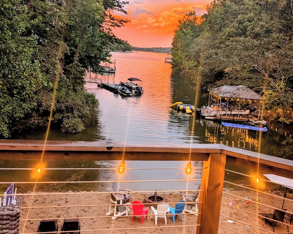 A lakeside deck with chairs and tables, overlooking a calm lake with boats and a dock.