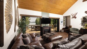 A spacious living area with a leather sofa, a fireplace, and a large window overlooking a deck.