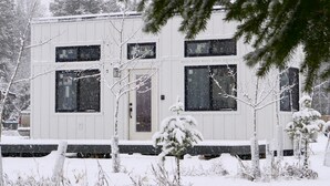 Een chalet met twee verdiepingen, een buitenkant bedekt met sneeuw, grote ramen en een duidelijke deur.