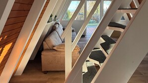 Ein Loft-Zimmer mit schrägverdeckter Decke, Holzbalken und einer Treppe mit Teppichstufen.