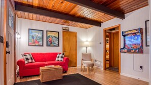 Una sala de estar acogedora con un sofá rojo, una cesta de mimbre, una lámpara y un juego de arcade.