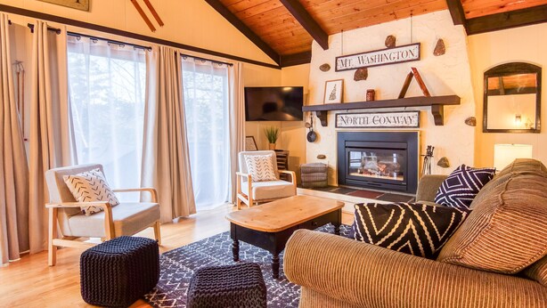 Un salón acogedor con chimenea, vigas de madera y una pared de piedra con letreros que dicen "Mt. Washington" y "North Conway".
