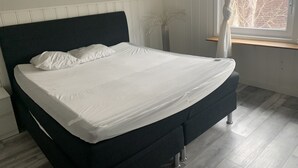 A bedroom with a bed, white bedding, a dark headboard, a window with curtains, and a potted plant. - Big Apartment in Stockholm City (Stockholm)