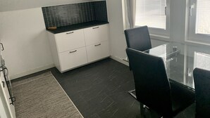A modern kitchen with a black countertop and white cabinets, a dining table with chairs, and a large window with blinds. - Big Apartment in Stockholm City (Stockholm)