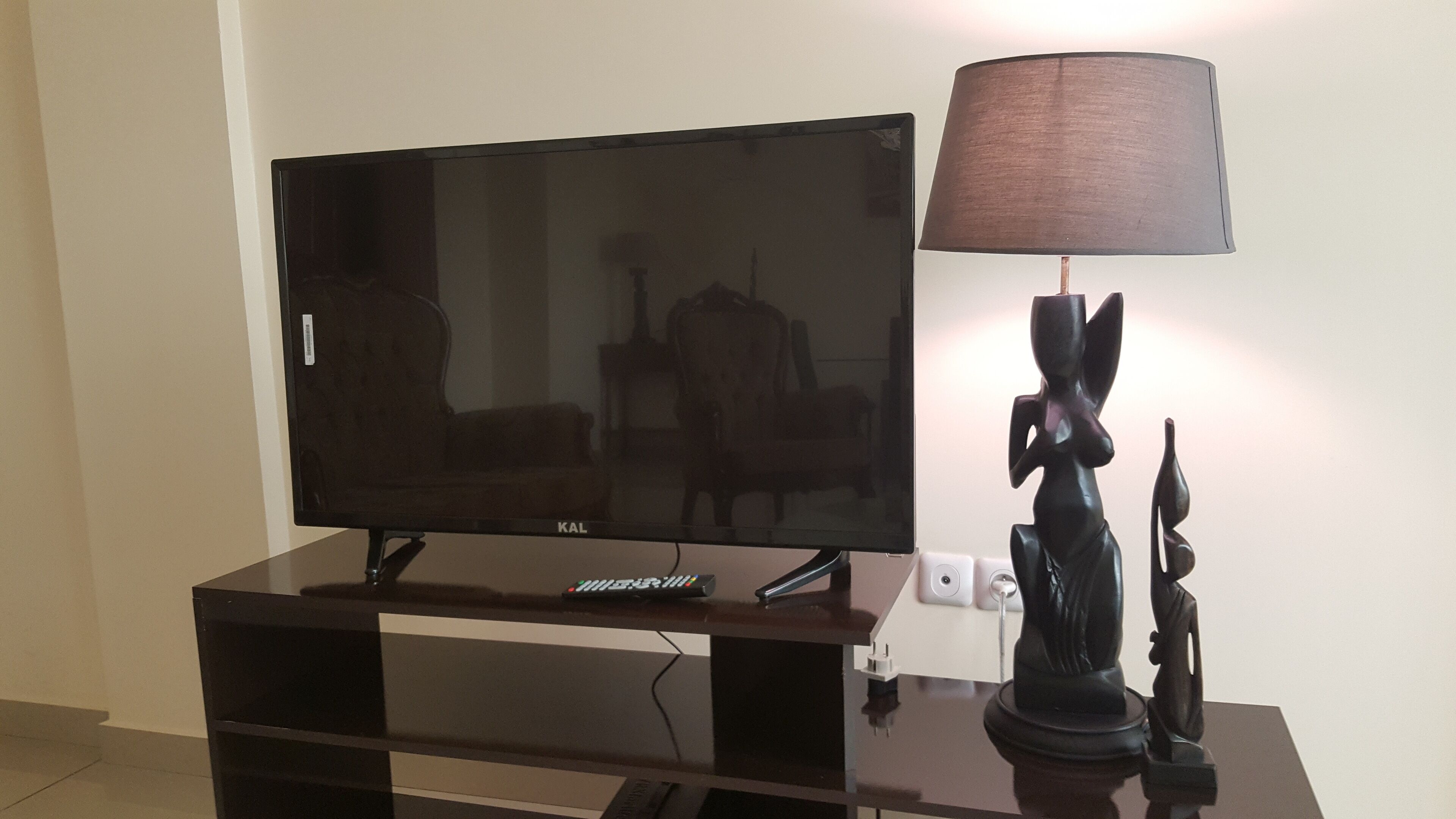A flat-screen TV on a wooden entertainment center with a remote control and a lamp.