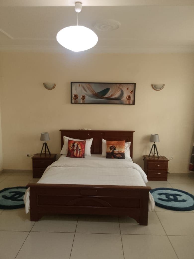 A bedroom with a wooden bed, two bedside tables with lamps, a ceiling light, and a wall-mounted painting.
