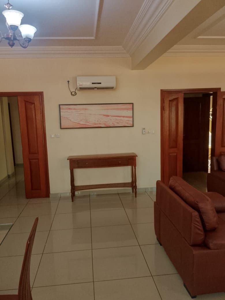 A room with a brown sofa, a wooden bench, a ceiling fan, and a wall-mounted air conditioner.