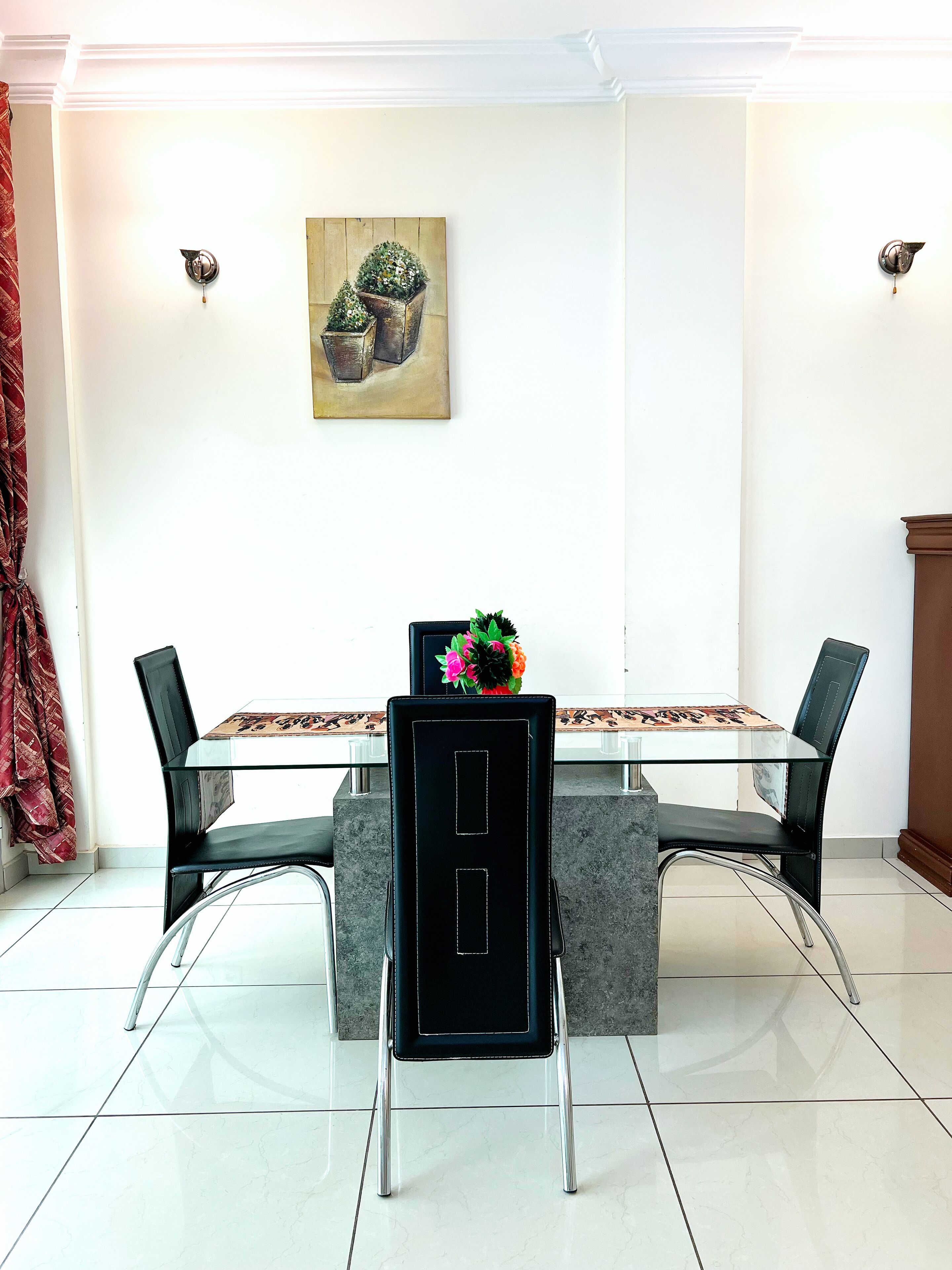 A dining area with a glass table, black chairs, and a small potted plant on the table.