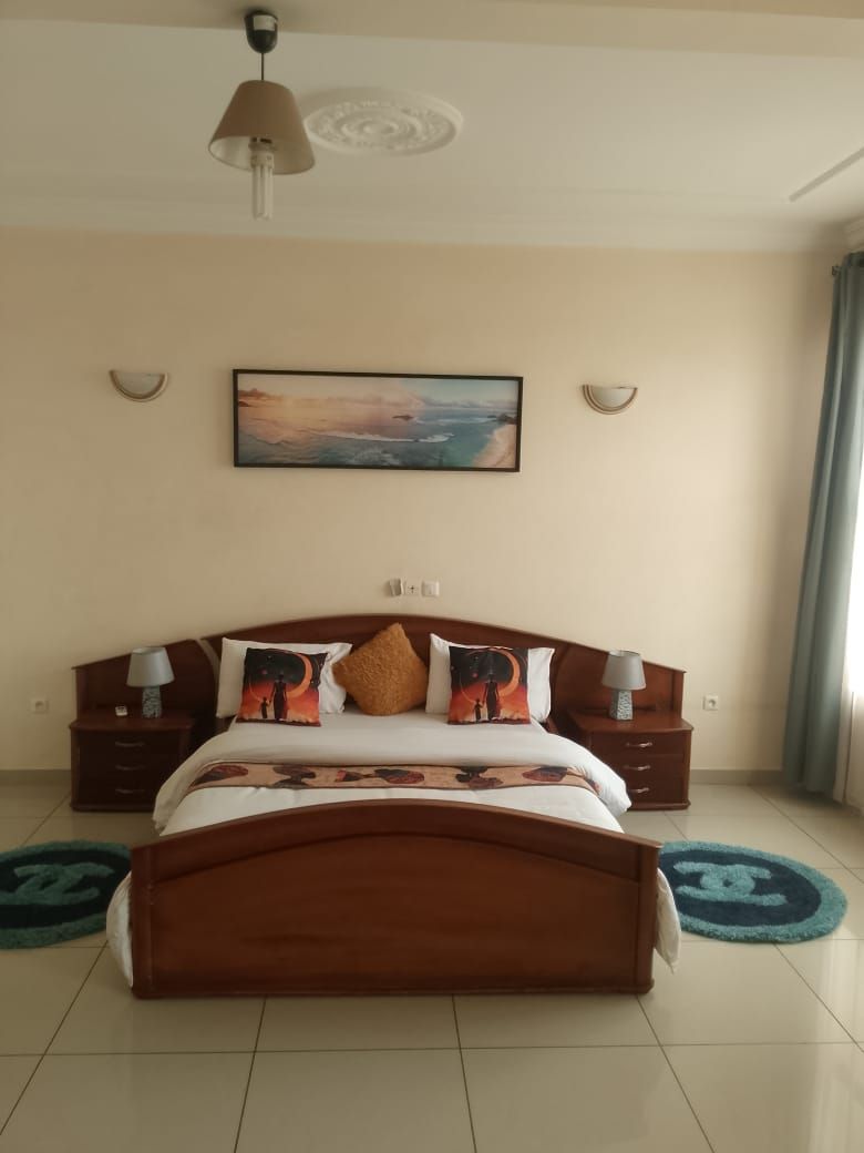A bedroom with a wooden bed, two bedside tables, a nightstand, a ceiling fan, a painting, and a window with curtains.