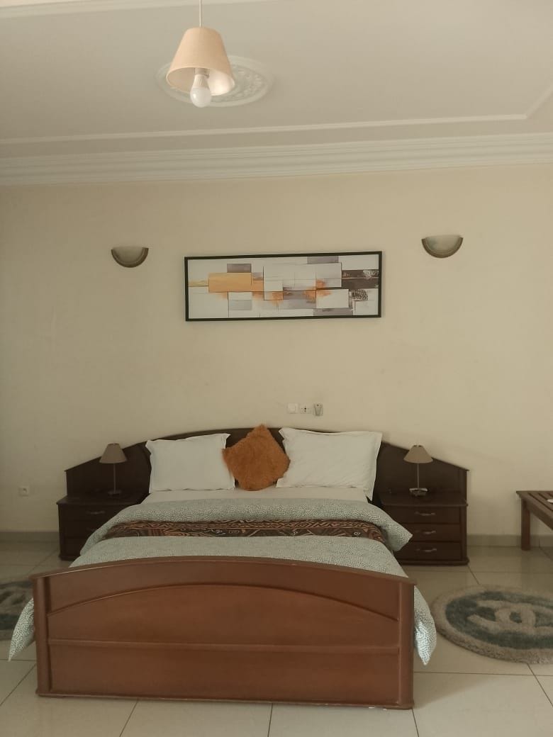 Un dormitorio con cama, mesitas de noche, lámpara, una obra de arte en la pared y luz de techo.