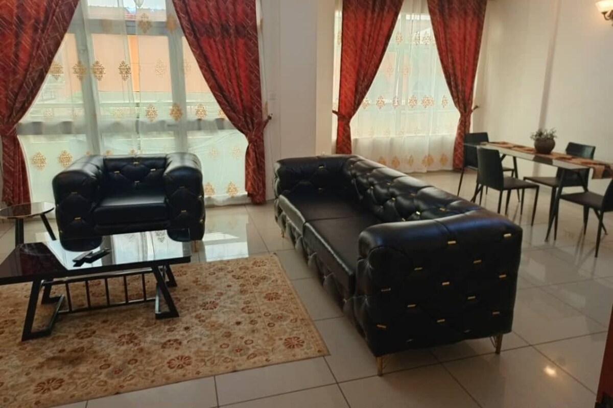 A living room with a black leather sofa, a glass coffee table, and a dining table with chairs.