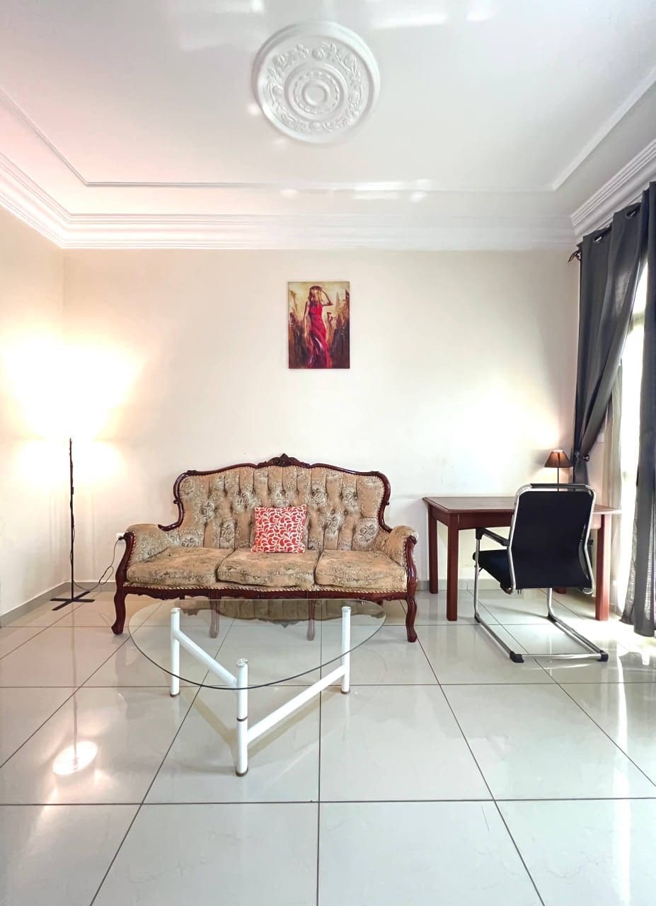 A room with a sofa, a table, a chair, a painting on the wall, and a ceiling with a decorative design.