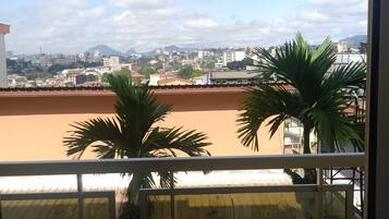 Un balcón con vista a un paisaje urbano, que incluye edificios y palmeras.