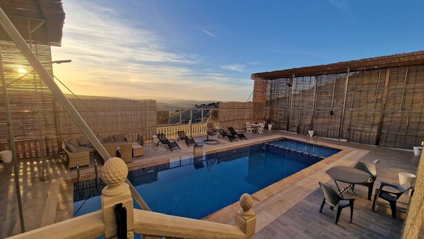 A rooftop pool area with a view of the landscape, furnished with lounge chairs and tables.