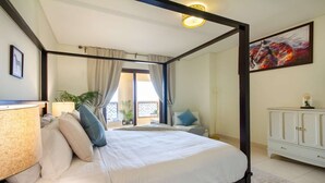 Een hemelbed met uitzicht op een balkon, een wit kastje en een schilderij aan de muur.