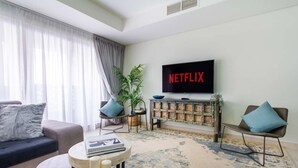 Een moderne woonkamer met een grote flatscreen-tv waarop 'NETFLIX' staat, een bank, twee fauteuils, een klein tafeltje met een boek en een decor kast.
