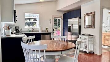 A modern kitchen with a central island, white cabinetry, and a dining area with a round table and white chairs.