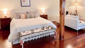 A bedroom with a bed, bedside tables, a chair, and a wooden beam structure. - Cozy Cabin in Redwoods | Hot Tub (Guerneville)