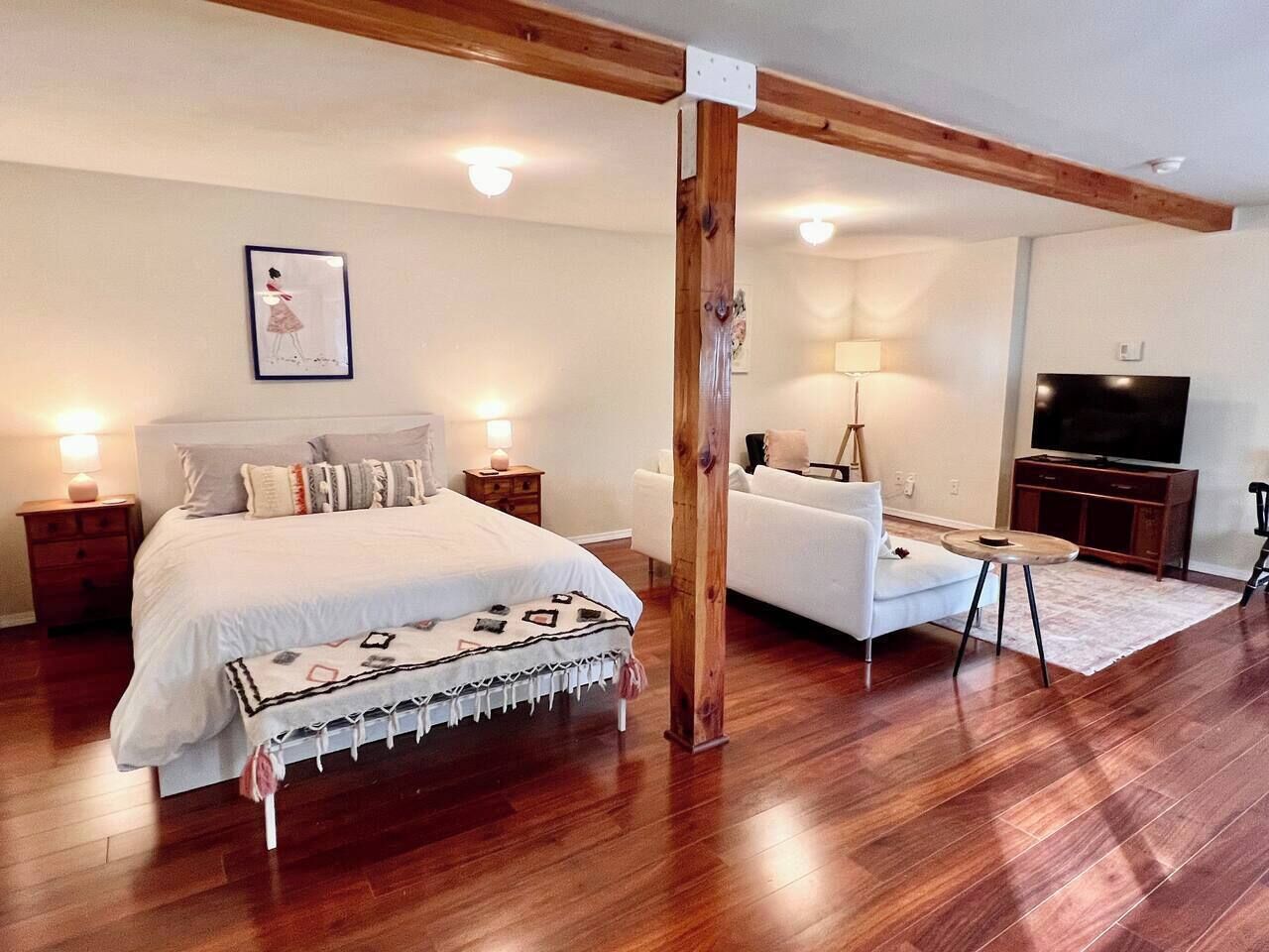 A bedroom with a bed, bedside tables, a sofa, a TV, and a wooden beam structure.