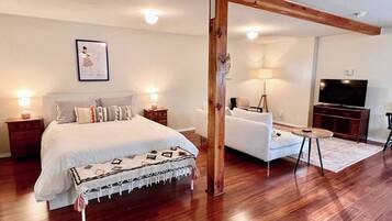 A bedroom with a bed, bedside tables, a sofa, a TV, and a wooden beam structure.