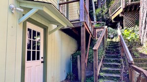 A wooden staircase leading to a door with a window, surrounded by greenery and a wooden deck. - Cozy Cabin in Redwoods | Hot Tub (Guerneville)