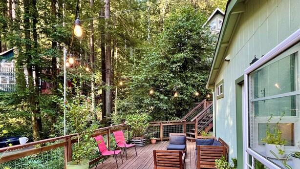 A wooden deck with outdoor seating, surrounded by lush greenery and a staircase leading to a building. - Cozy Cabin in Redwoods | Hot Tub (Guerneville)
