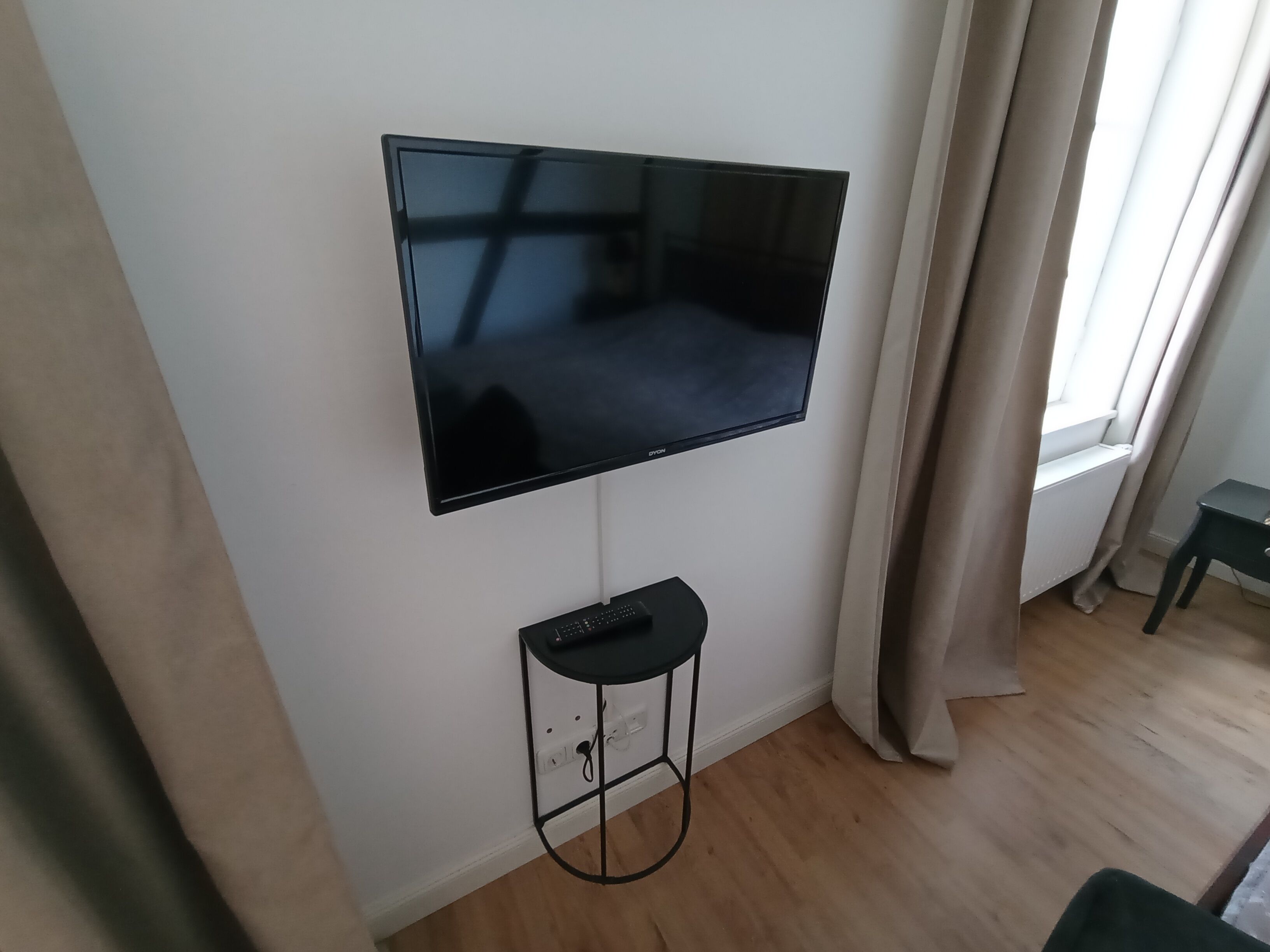 Un televisor de pantalla plana montado en una pared, con un control remoto sobre un pedestal debajo.