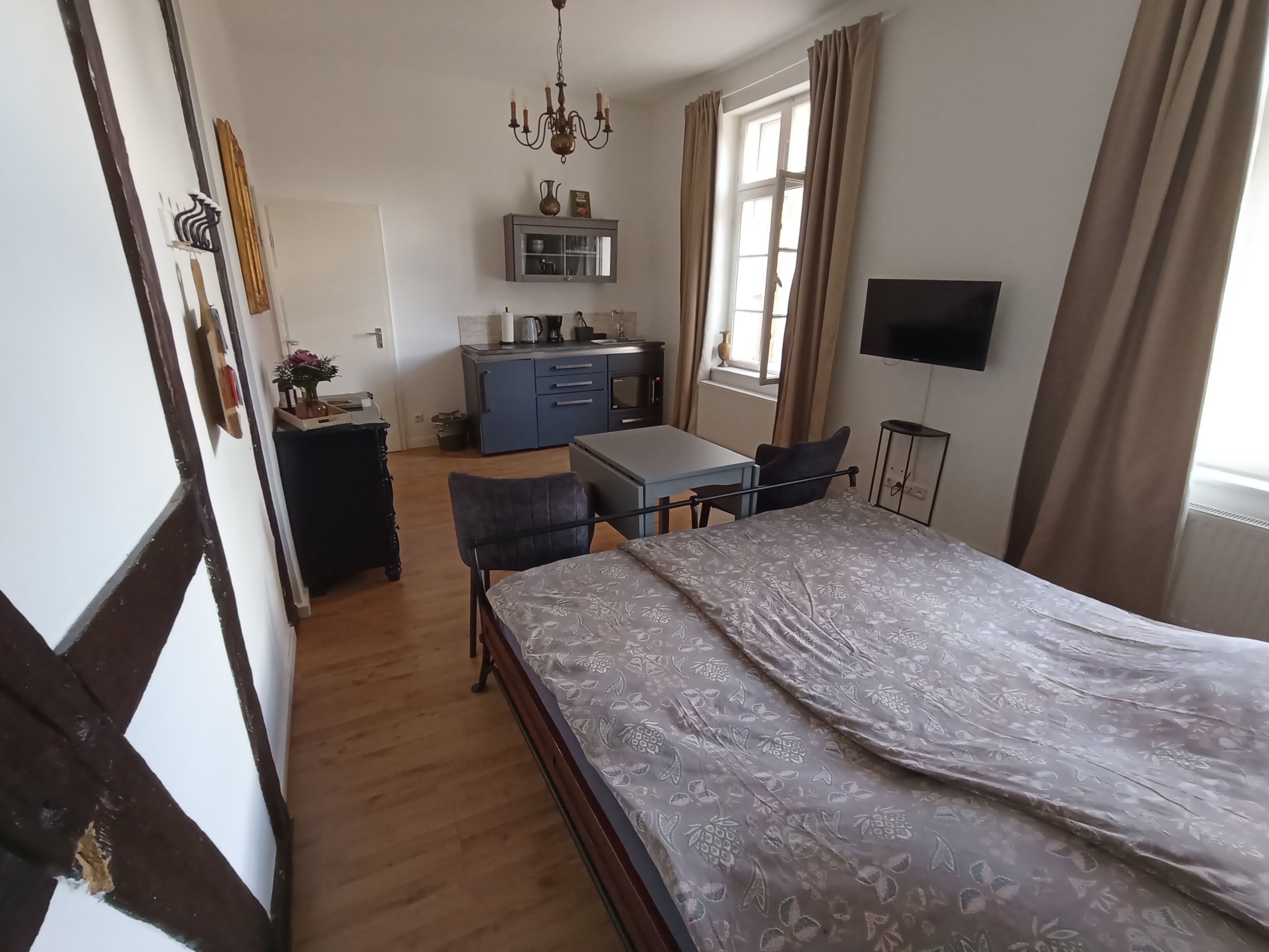 Quarto com cama, escrivaninha, cadeira, televisão e cozinha compacta.