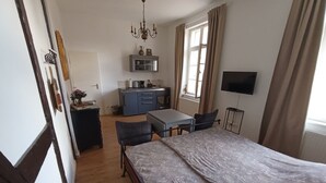 Een slaapkamer met een bed, een bureau, een stoel, een televisie en een kitchenette.