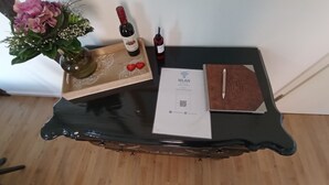 Une petite table sur laquelle se trouve un plateau avec une bouteille de vin, un vase de fleurs, un verre à vin, un petit livret et un code QR.