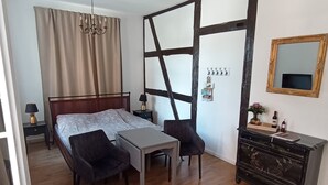Een slaapkamer met een bed, een bureau, een stoel, een dressoir, een spiegel en een kroonluchter.