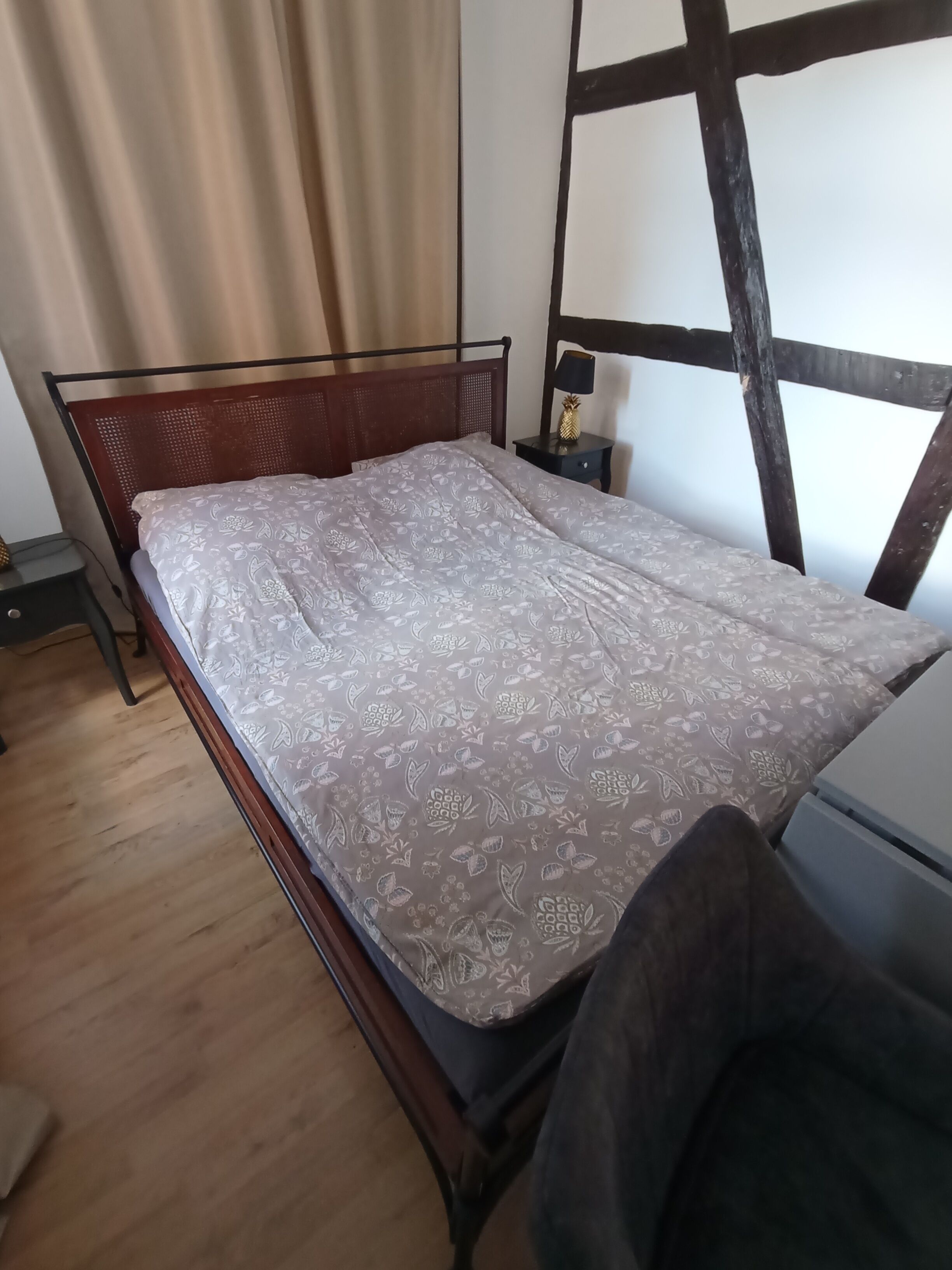A single bed with a patterned bedspread, a wooden headboard, a nightstand with a lamp, and a window with a curtain.