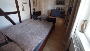 Een slaapkamer met een bed, een bureau en een stoel. In de verte is een kitchenette te zien.