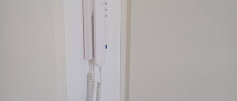 A white wall-mounted telephone with a corded handset and a separate base unit.