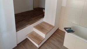 Un intérieur moderne avec un escalier menant à un deuxième étage, un coin cuisine doté de meubles blancs et un plancher en bois.