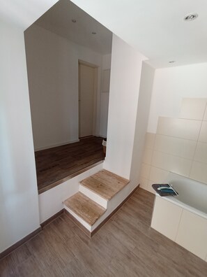 Un interior moderno con una escalera que lleva a un segundo piso, una zona de cocina con armarios blancos y piso de madera.