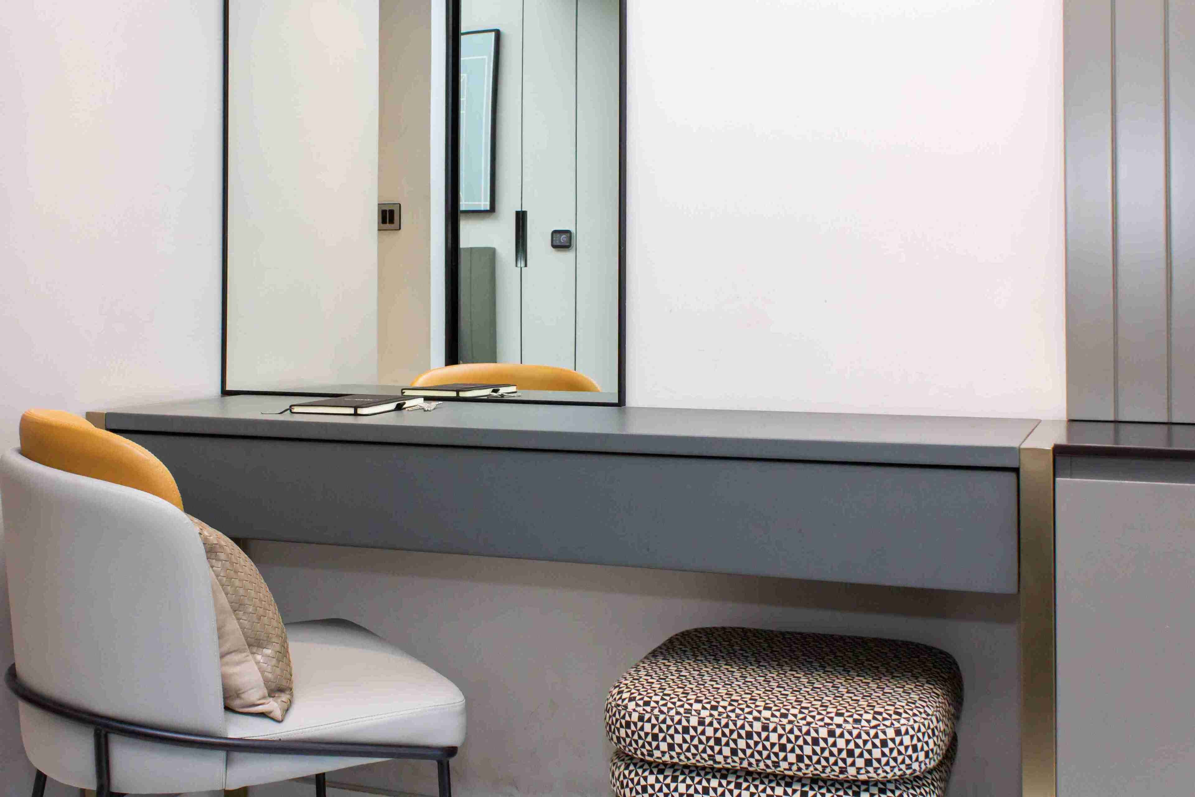 A modern bathroom with a large mirror, a white chair with a beige cushion, and a patterned stool.