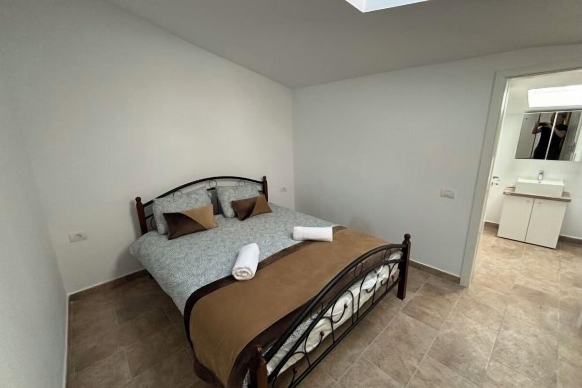 Un dormitorio con cama, un baño con espejo y lavamanos, y suelo de baldosas.