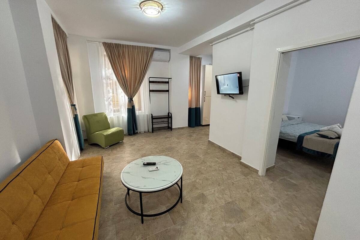A modern hotel room with a sofa, a round table, a TV, and a bed.