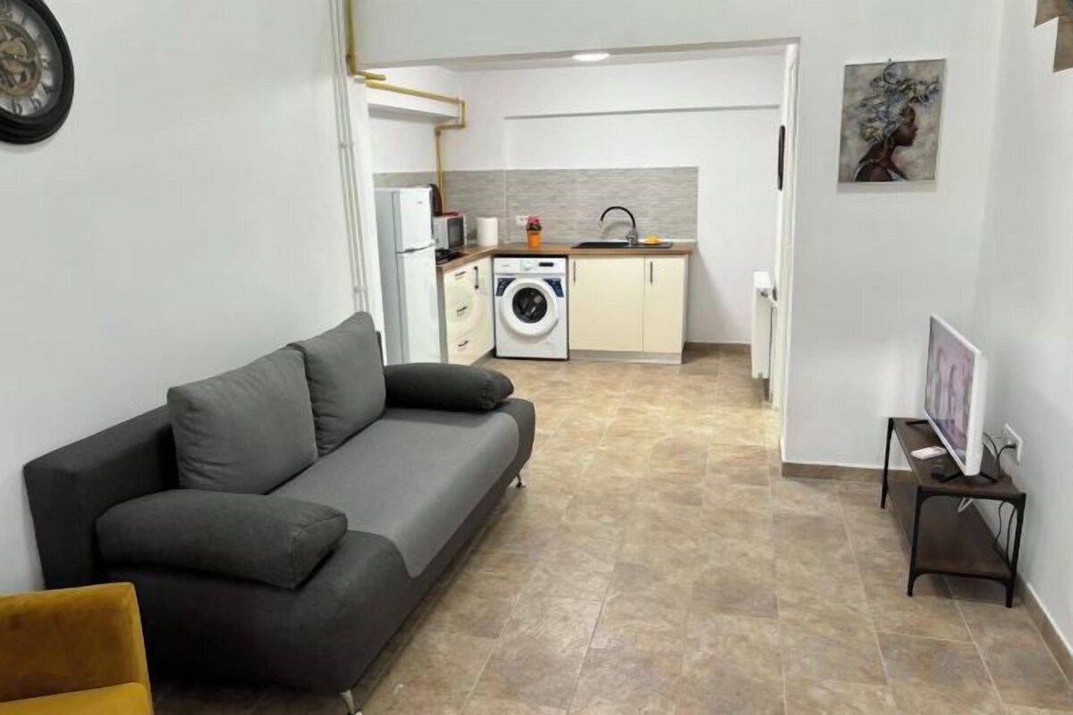 Una sala de estar con sofá, lavadora y cocina al fondo.