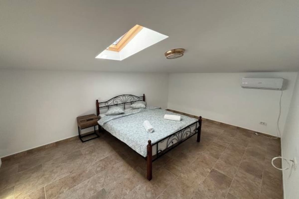 A bedroom with a bed, a bedside table, a ceiling light fixture, and an air conditioning unit.