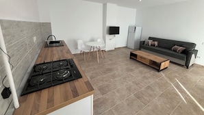 A modern kitchen with a wooden countertop and gas stove, a dining area with a white table and chairs, a grey sofa, and a television mounted on the wall. - The Loft Gara de Nord (Bucharest)