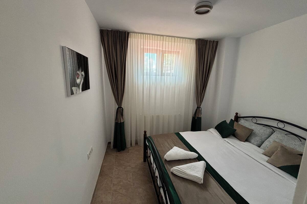 A bedroom with a bed, curtains, a radiator, and a wall-mounted picture.