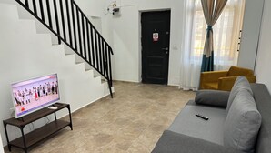 A living room with a grey sofa, a TV on a stand, a staircase, and a door with a 'No Smoking' sign. - The Loft Gara de Nord (Bucharest)